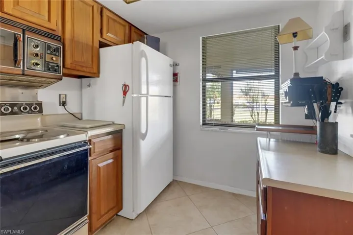 Kitchen featuring hanging light fixtures, light tile patterned floors, white refrigerator, and electric stove