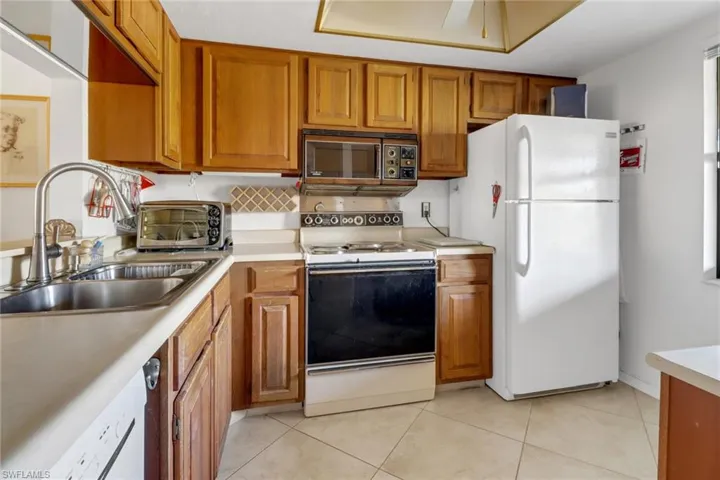 Kitchen featuring sink, white appliances, ceiling fan, and light tile patterned flooring