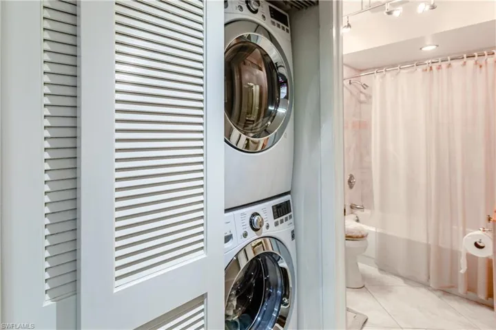 Clothes washing area with stacked washing maching and dryer and light tile patterned floors
