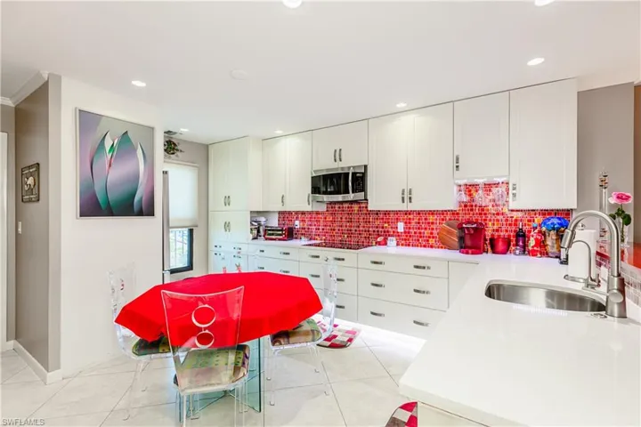 Kitchen with white cabinetry, sink, backsplash, stovetop, and light tile patterned floors