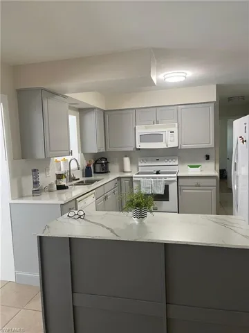 Kitchen with gray cabinetry, white appliances, light tile patterned flooring, and light stone counters