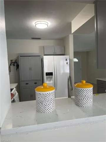 Kitchen with gray cabinets, white refrigerator with ice dispenser, light stone counters, and a peninsula
