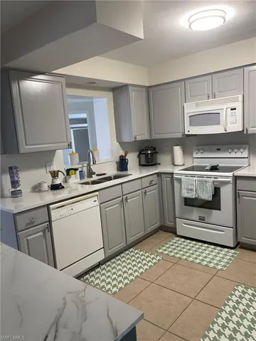 Kitchen featuring gray cabinets, white appliances, light tile patterned flooring, and light stone countertops