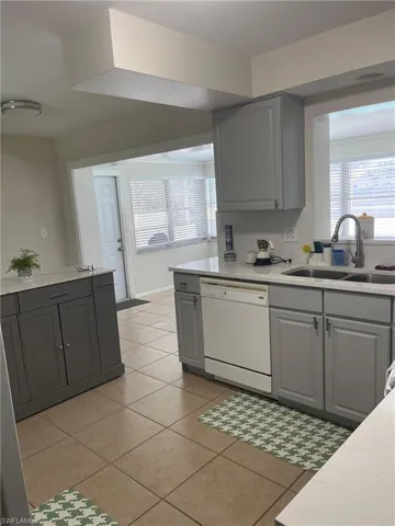 Kitchen with gray cabinetry, light tile patterned floors, dishwasher, and healthy amount of natural light