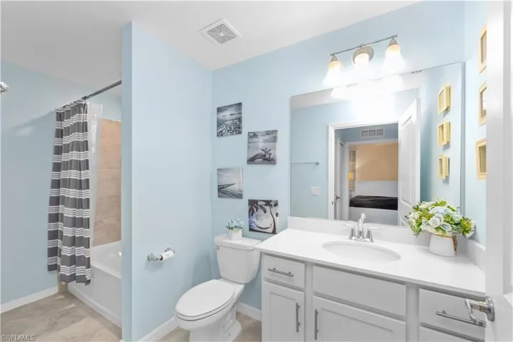Full bathroom with vanity, shower / tub combo, toilet, and visible vents