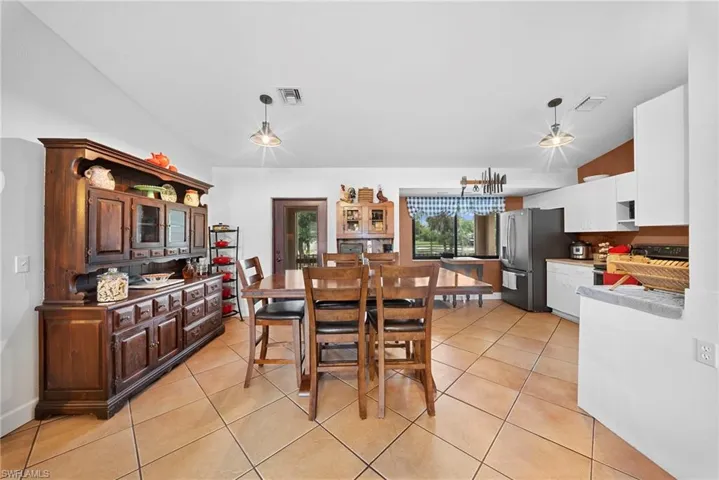 Open-concept living area featuring a kitchen with white cabinetry and dark appliances, a dining space with tiled flooring, and a large window overlooking exterior scenery