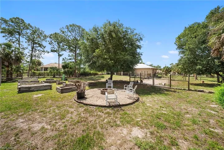 Expansive outdoor area featuring a circular fire pit area with paver edging, mature trees, and multiple raised garden beds