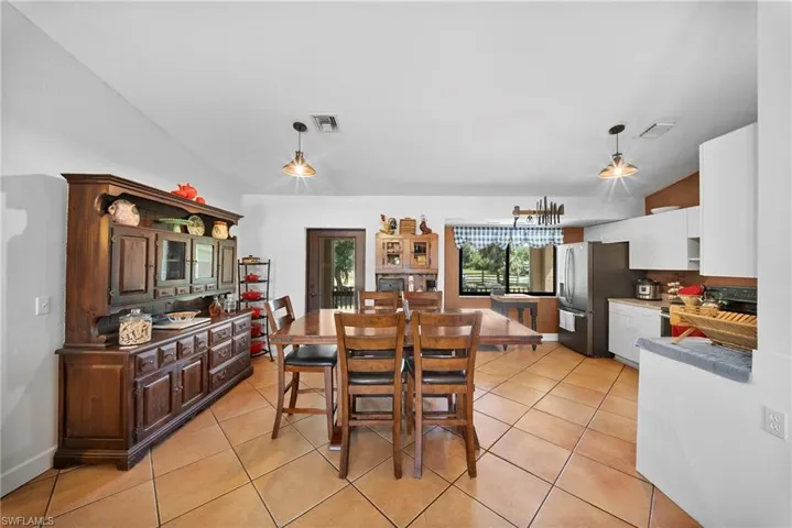 Open-concept dining and kitchen area featuring tile flooring, white shaker cabinetry, stainless steel appliances, and a window overlooking exterior landscaping