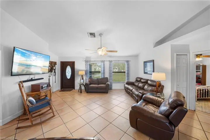 Open-concept living space featuring high vaulted ceilings, light-toned tile flooring, and a ceiling fan with integrated lighting