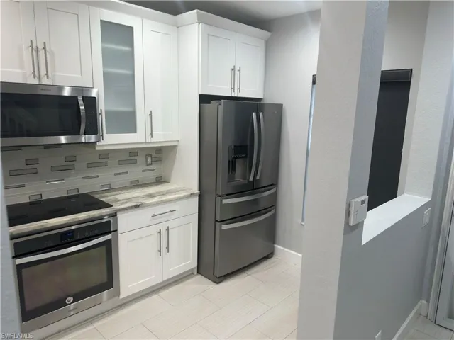Kitchen with appliances with stainless steel finishes, tasteful backsplash, white cabinetry, light stone countertops, and glass insert cabinets