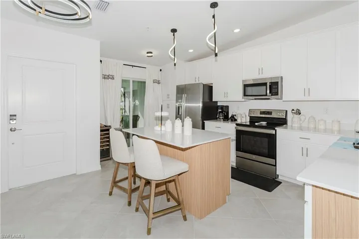 Kitchen featuring appliances with stainless steel finishes, a kitchen island, a breakfast bar area, white cabinetry, and light countertops