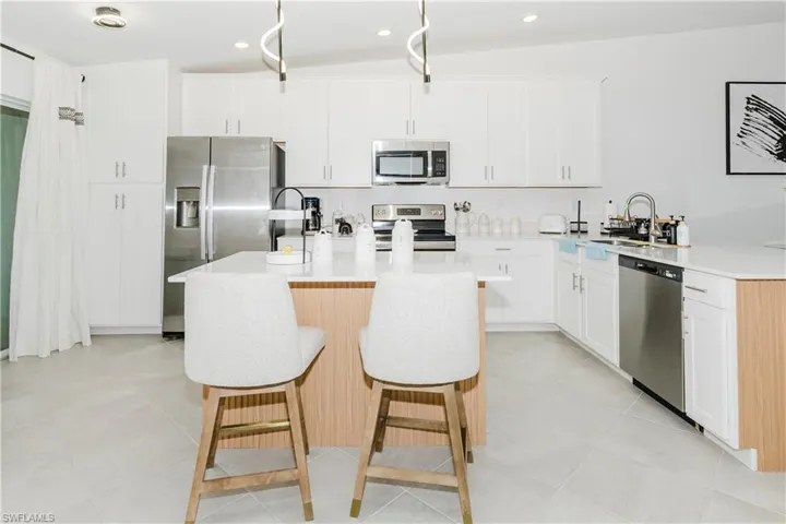 Kitchen with stainless steel appliances, a breakfast bar, light countertops, a kitchen island with sink, and recessed lighting