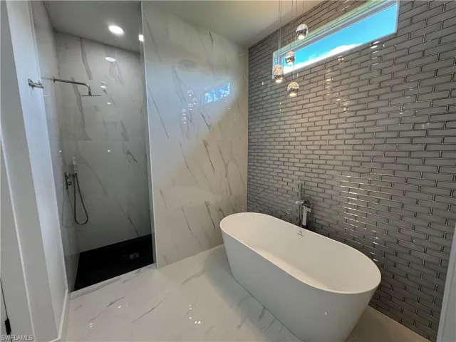 Freestanding soaking tub, floor-to-ceiling large-format wall tile, glass-enclosed shower with rainfall showerhead, and a grey brick-patterned accent wall with clerestory window