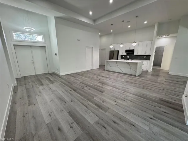 Open-concept interior featuring wood-finish flooring, high ceilings with recessed lighting, white shaker-style cabinetry, and a kitchen island with a stone-finish countertop