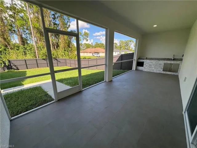 Screened lanai featuring tile flooring, built-in outdoor kitchen with stone veneer base, and access to a fenced backyard
