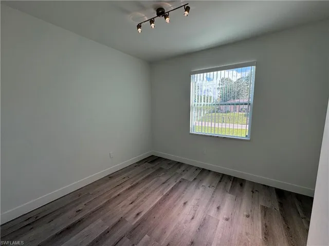 Neutral wall finish, wood-finish flooring, multi-directional track lighting, and vertical window blinds