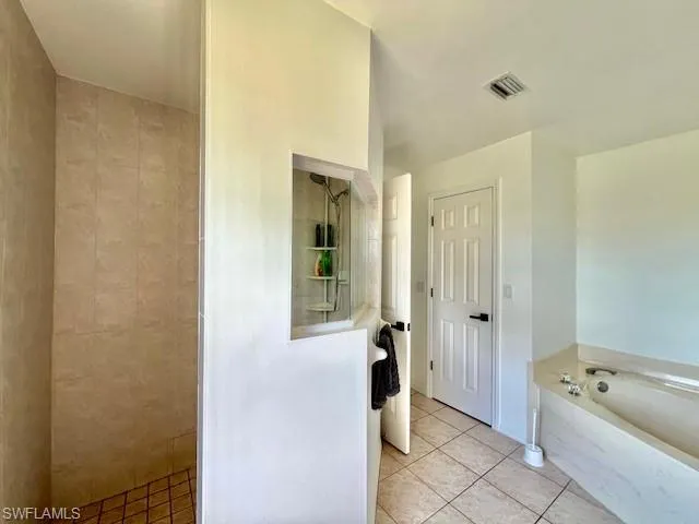 Bathroom with light tile patterned floors, a garden tub, and a tile shower