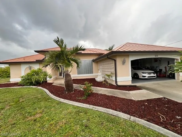 View of front facade with stucco siding, driveway, a metal roof, a front yard, and a standing seam roof