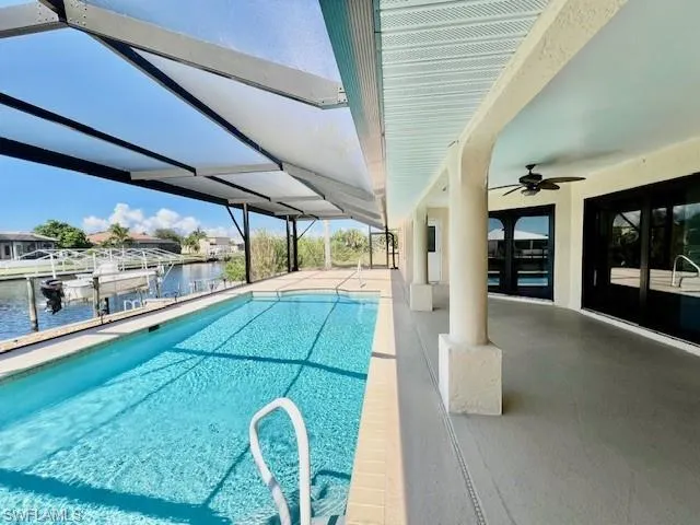 Outdoor pool with a patio area, a water view, ceiling fan, boat lift, and a dock