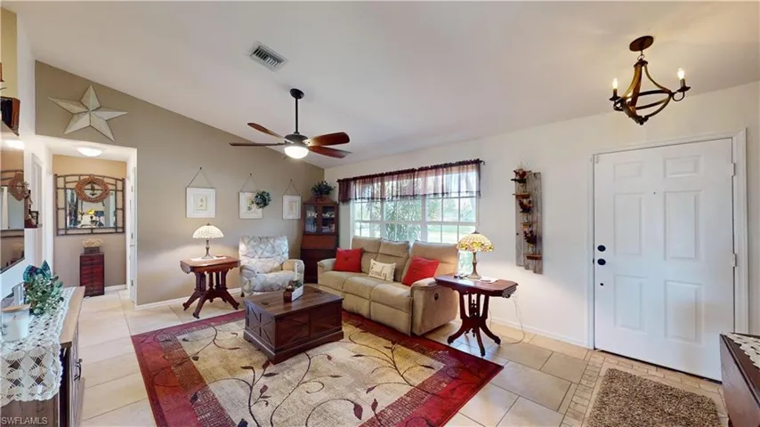 Tiled living room featuring lofted ceiling and ceiling fan with notable chandelier