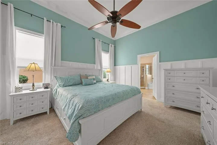 Bedroom with a wainscoted wall, ornamental molding, connected bathroom, a decorative wall, and light colored carpet