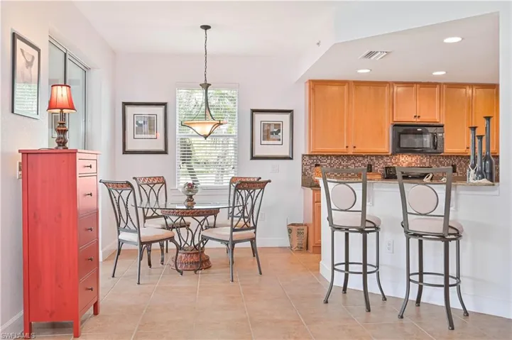 Kitchen featuring a breakfast bar, black microwave, backsplash, a peninsula, and dark stone countertops