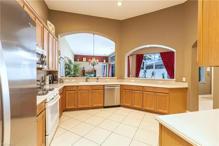Kitchen with a chandelier, appliances with stainless steel finishes, light tile patterned floors, brown cabinets, and light countertops