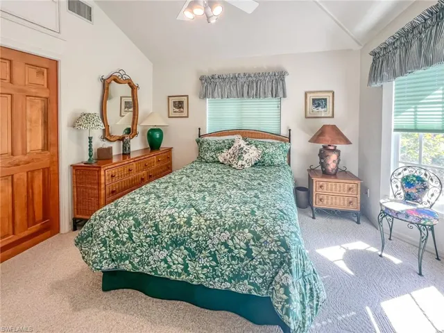 Carpeted bedroom with ceiling fan, visible vents, and vaulted ceiling
