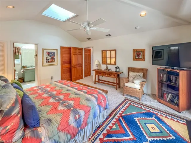 Carpeted bedroom featuring vaulted ceiling with skylight, a closet, visible vents, and connected bathroom
