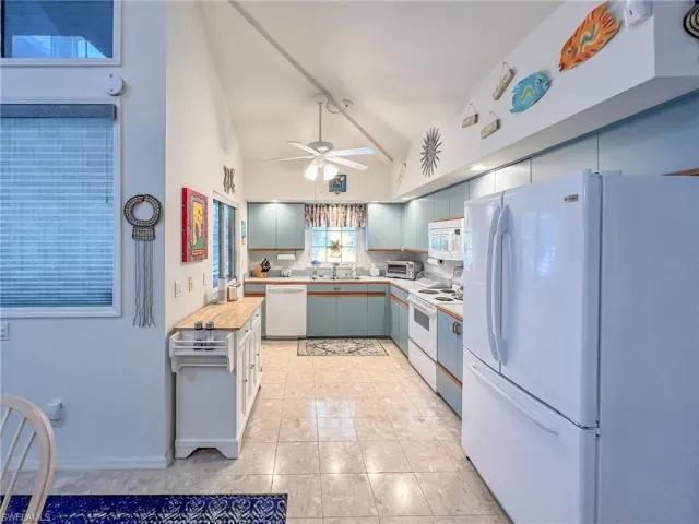 Kitchen featuring light countertops, a ceiling fan, vaulted ceiling, a sink, and white appliances