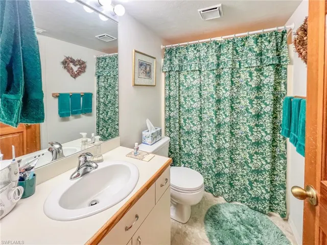 Bathroom with a shower with curtain, visible vents, vanity, and toilet