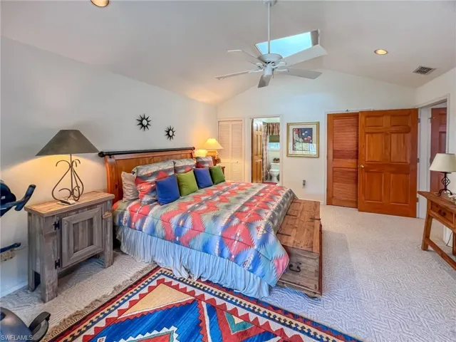 Bedroom with visible vents, a ceiling fan, connected bathroom, lofted ceiling, and carpet floors