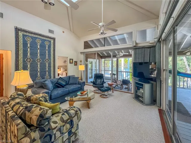 Living area with high vaulted ceiling, carpet, visible vents, and a ceiling fan