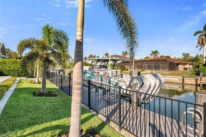 Surrounding community with a water view, a dock, fence, and a yard