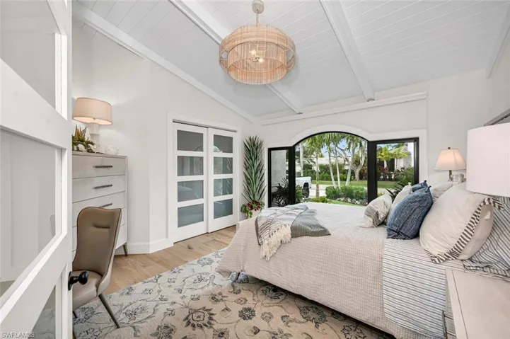 Bedroom with vaulted ceiling with beams, an inviting chandelier, access to exterior, and wood finished floors
