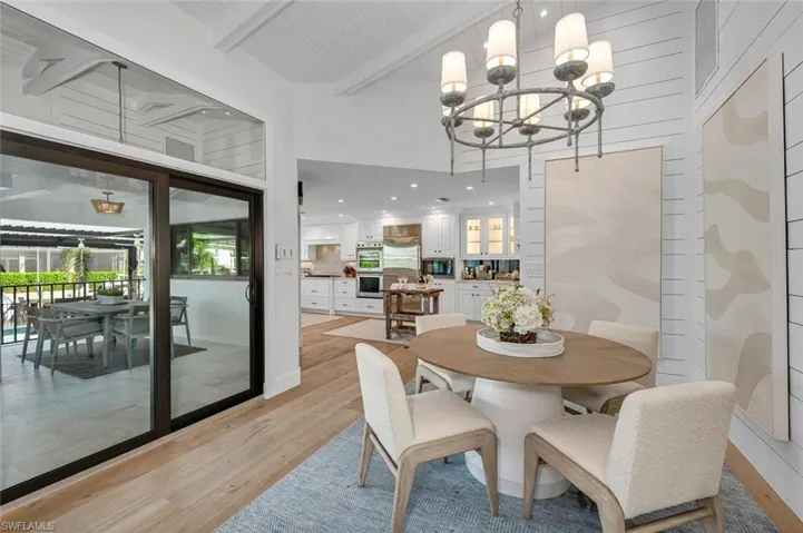 Dining space with light wood finished floors, beamed ceiling, a high ceiling, and a notable chandelier