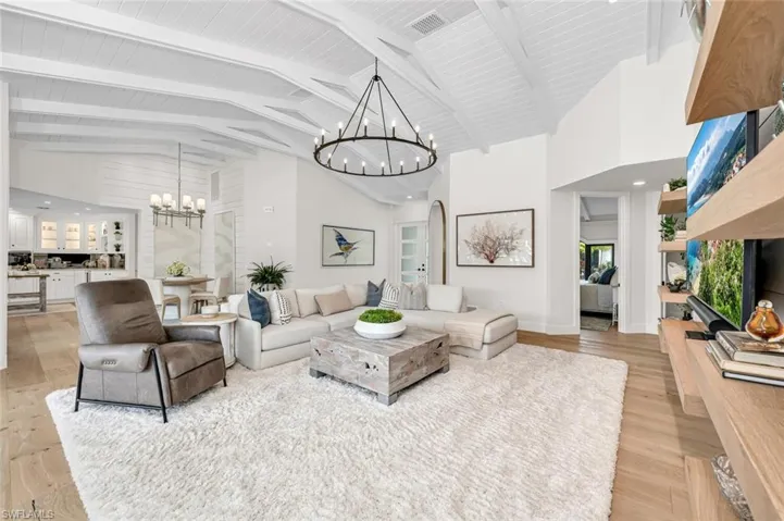 Living room with light wood-type flooring, high vaulted ceiling, visible vents, and a chandelier