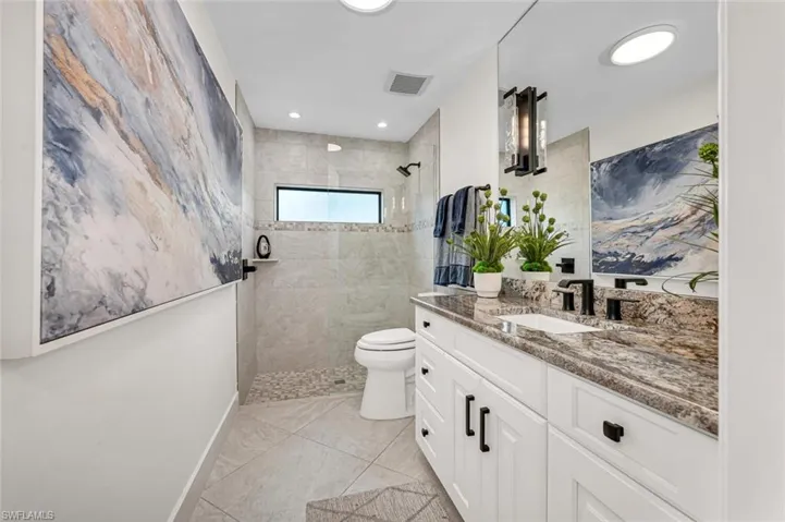Full bath with visible vents, toilet, vanity, baseboards, and walk in shower