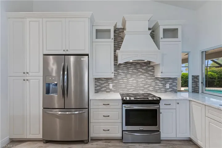 Kitchen featuring lofted ceiling, custom range hood, appliances with stainless steel finishes, and white cabinetry