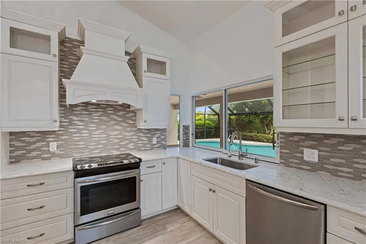 Kitchen featuring vaulted ceiling, appliances with stainless steel finishes, white cabinets, and tasteful backsplash