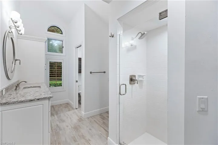 Bathroom featuring vanity, vaulted ceiling, hardwood / wood-style floors, and a shower with shower door