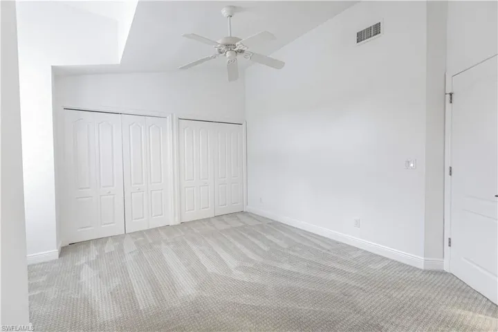 Unfurnished bedroom with ceiling fan, light carpet, high vaulted ceiling, and multiple closets