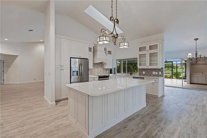 Kitchen featuring premium range hood, hanging light fixtures, stainless steel appliances, a center island, and white cabinetry