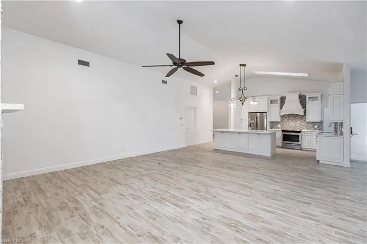 Unfurnished living room featuring light wood-type flooring, ceiling fan, sink, and vaulted ceiling