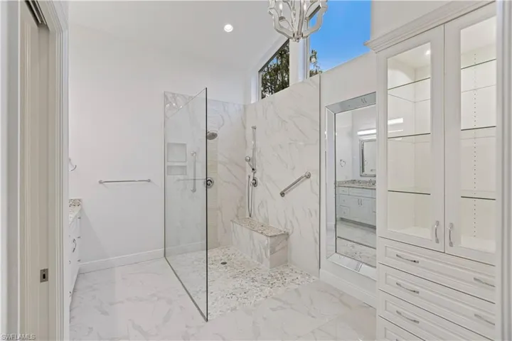 Bathroom featuring tiled shower, an inviting chandelier, and vanity