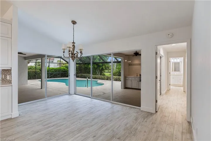 Unfurnished dining area featuring ceiling fan with notable chandelier, light wood-type flooring, vaulted ceiling, and plenty of natural light
