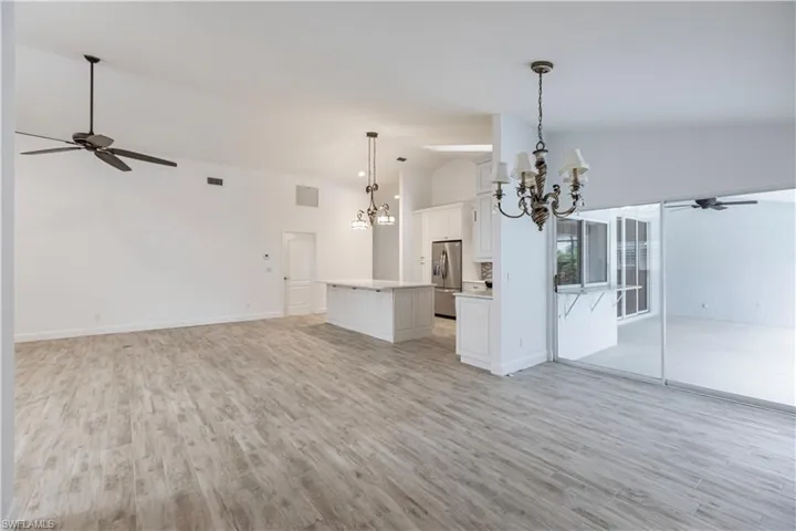 Unfurnished living room with ceiling fan with notable chandelier, high vaulted ceiling, and light hardwood / wood-style floors