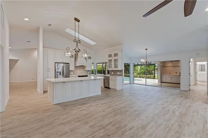 Kitchen featuring white cabinets, decorative light fixtures, ceiling fan with notable chandelier, stainless steel appliances, and a kitchen island