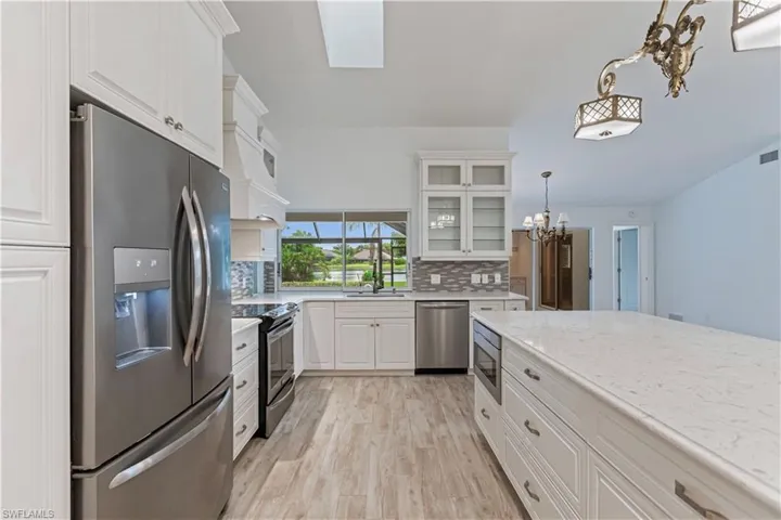 Kitchen featuring appliances with stainless steel finishes, white cabinetry, light stone counters, and tasteful backsplash
