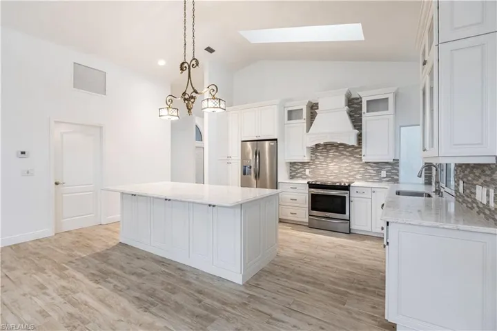 Kitchen with a kitchen island, lofted ceiling with skylight, custom range hood, appliances with stainless steel finishes, and sink